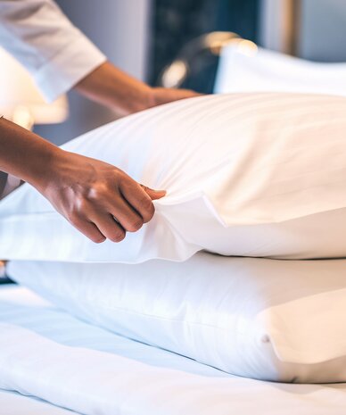 Person arranging pillows on a neatly made bed.
