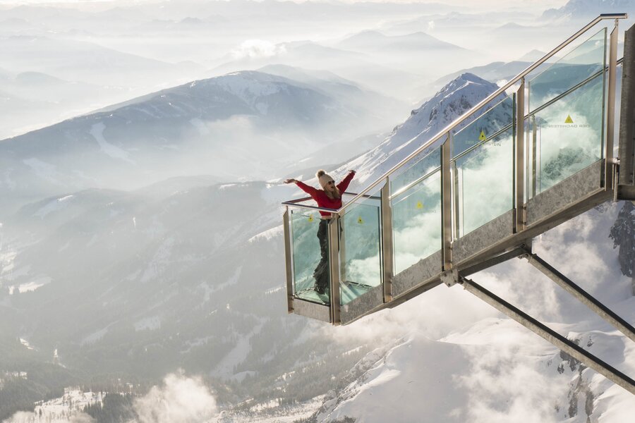 Person on glass skywalk extending over snow-capped mountains