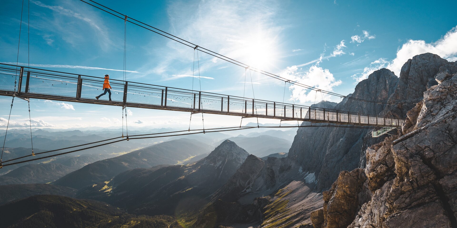 Suspension bridge across a rocky mountain valley with hiker