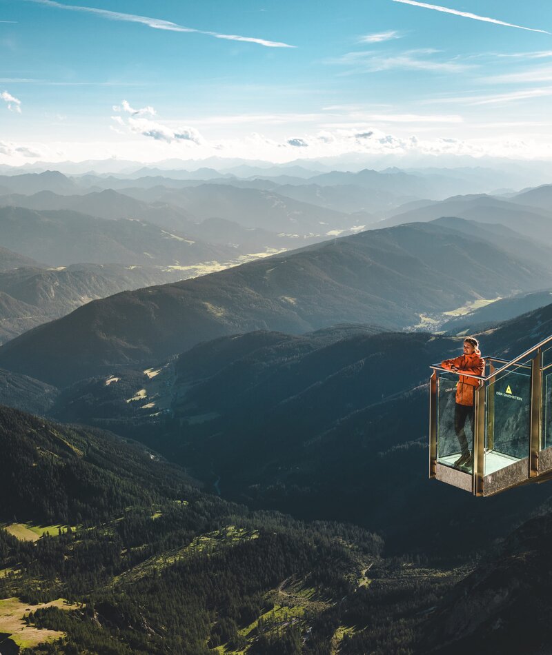 Person in orange jacket on glass viewing platform over mountains