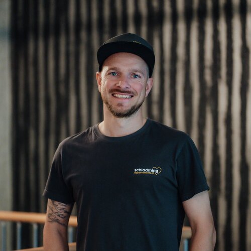 Smiling man in a black t-shirt with a chest logo indoors