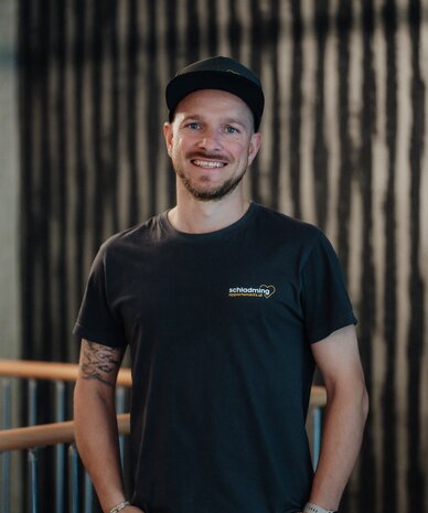 Smiling man in a black t-shirt with a chest logo indoors