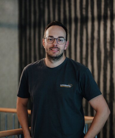 Man with glasses in dark T-Shirt posing indoors by railing.