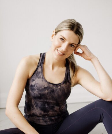 Smiling woman in athletic wear sits on yoga mat