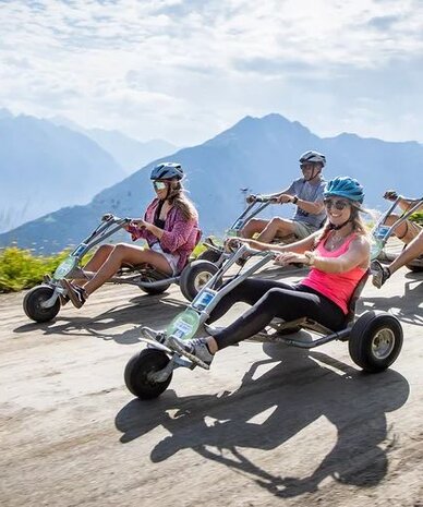 Group of four wearing helmets riding pedal go-karts on mountain road