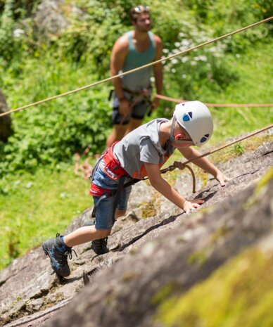 Child wearing helmet climbs a rocky wall with rope