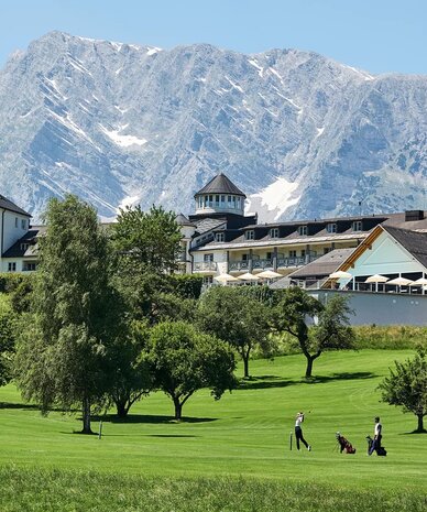 Green golf course with trees and mountain backdrop