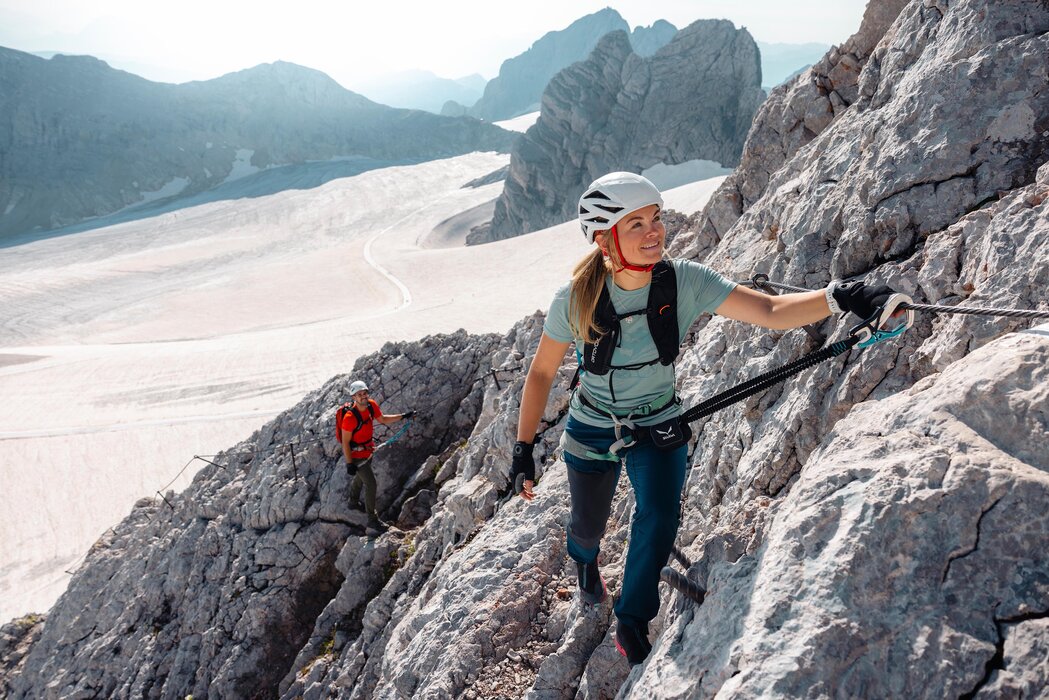 Two climbers ascend a snow-dusted mountain ridge with helmets