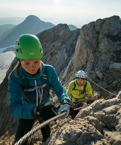 Two climbers ascend a rocky mountain ridge using a rope