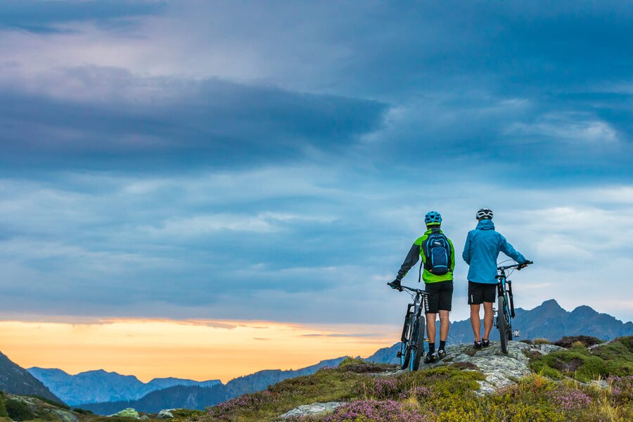 Two cyclists with mountain bikes on a rocky ridge at sunset