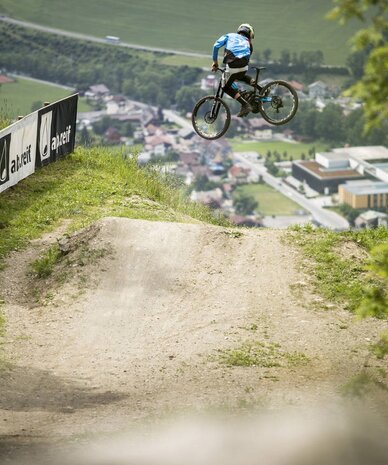 Mountain biker mid-air jump on dirt track hillside | © Roland Haschka/Young Mountain Marketing