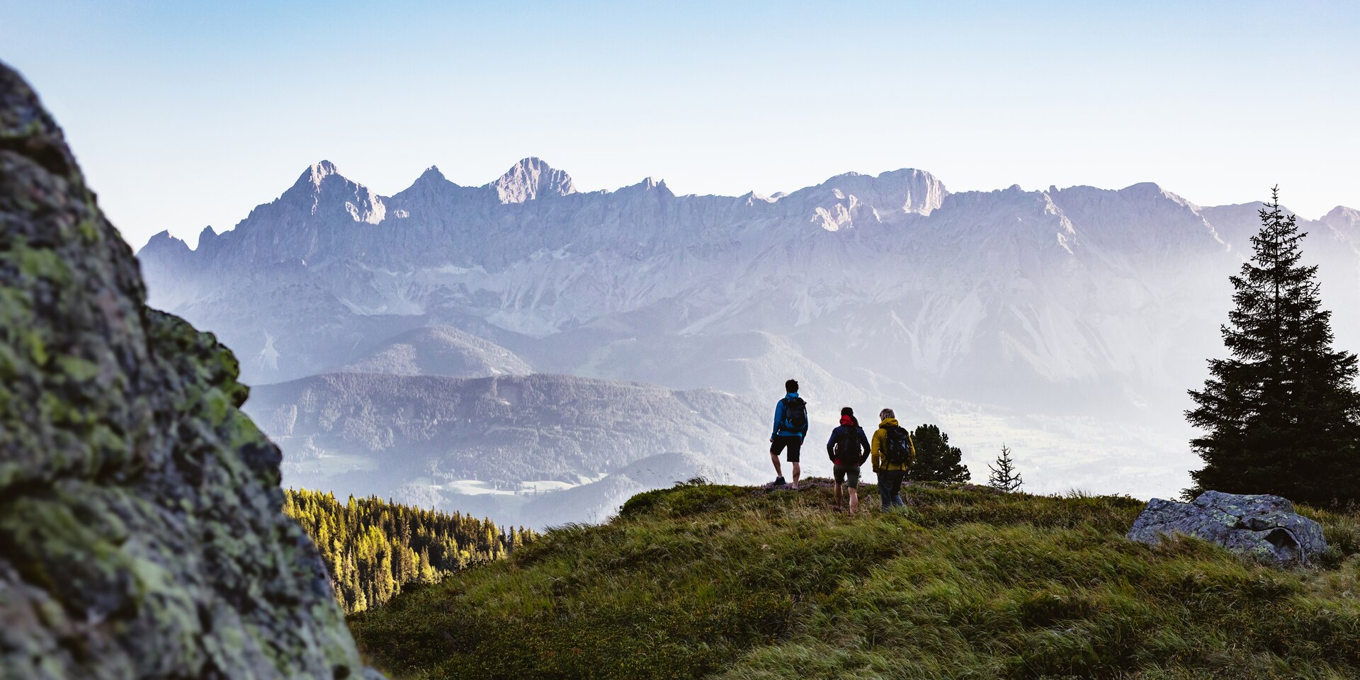 Group of hikers on grassy overlook facing distant mountains | © Sebastian Stiphout