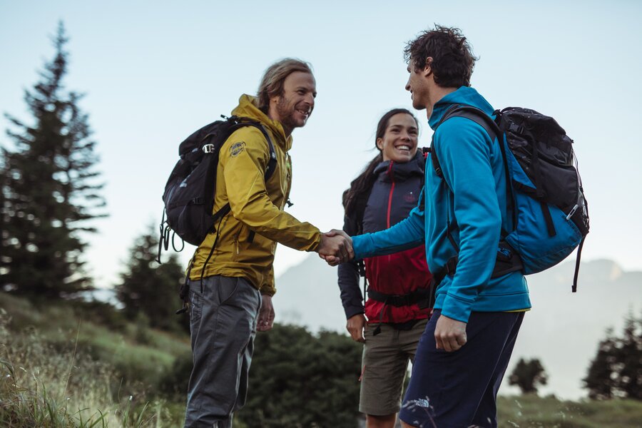 Three hikers with backpacks shake hands outdoors | © Sebastian Stiphout