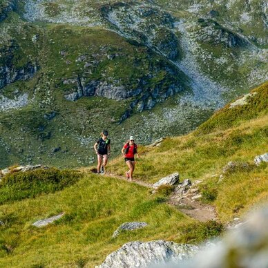 Two hikers walk along a narrow mountain path.