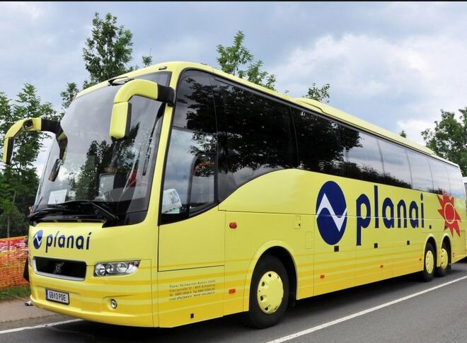 Yellow coach bus with Planai logo parked on the road