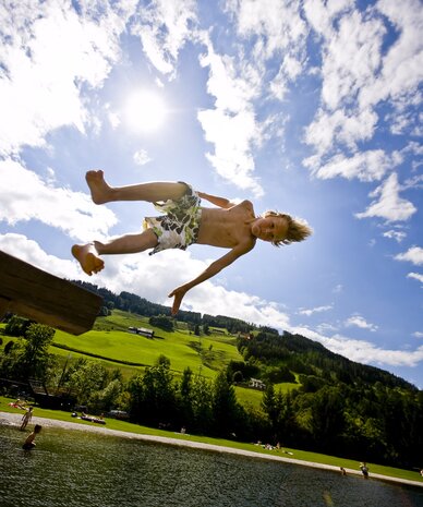 Young boy jumps from diving board into lake | © Tom Lamm