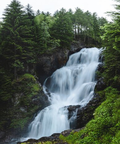 Tall waterfall cascading through a green forest canyon