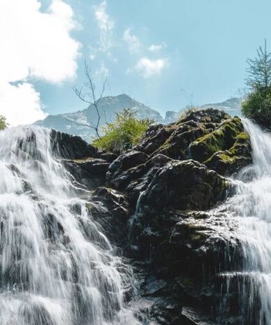 Waterfall cascading over rocky ledges amid green foliage and blue sky