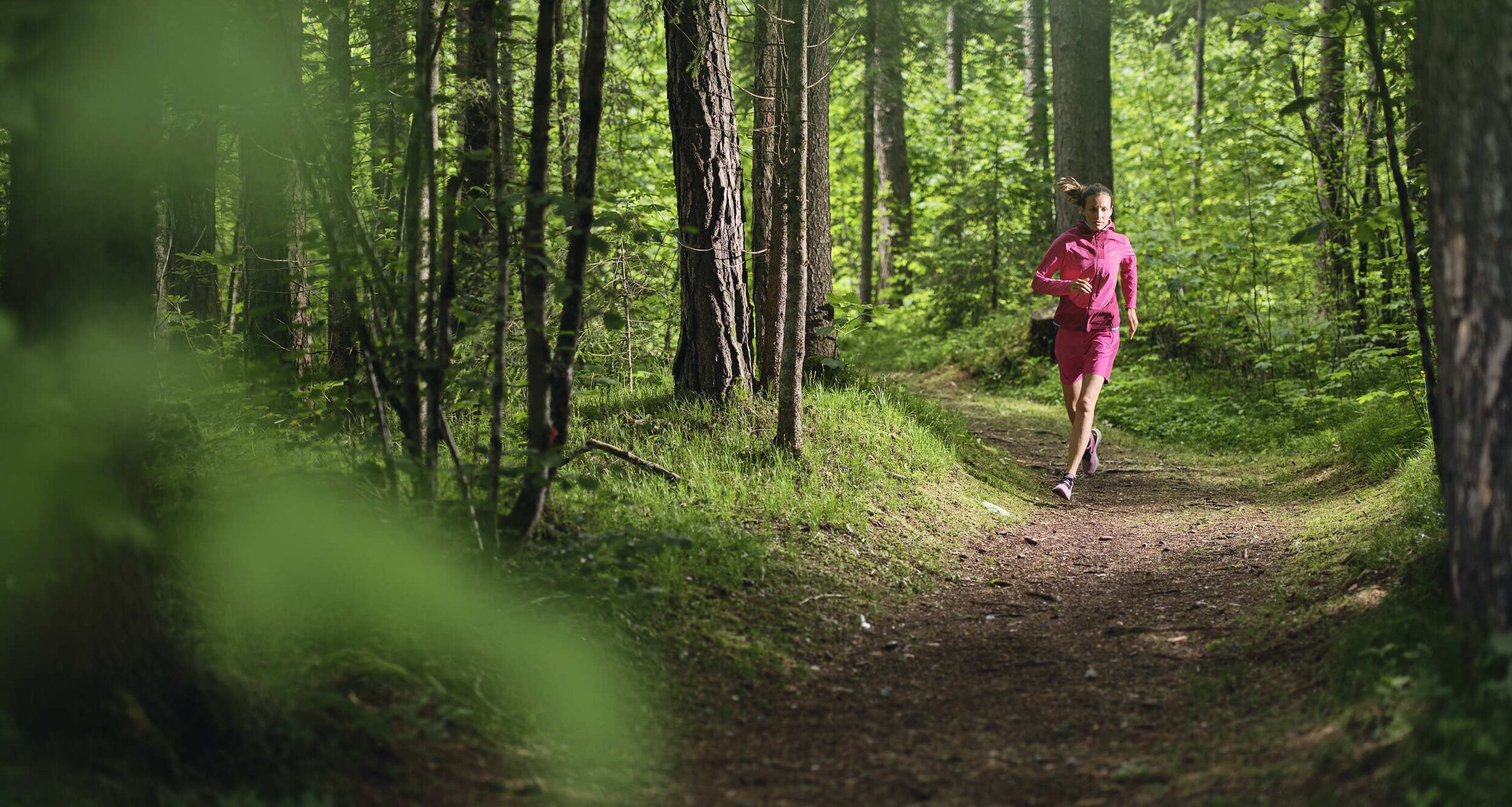 Frau joggt in pinkem Outfit auf Waldweg | © RAPHAELGABAUER.COM