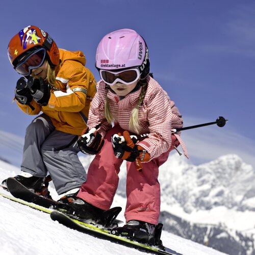 Two children with helmets and goggles snowboarding down a snowy slope | © Tom Lamm