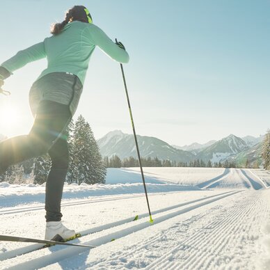 Skier in green jacket gliding on cross-country skis through sunlit snow | © Peter Burgstaller