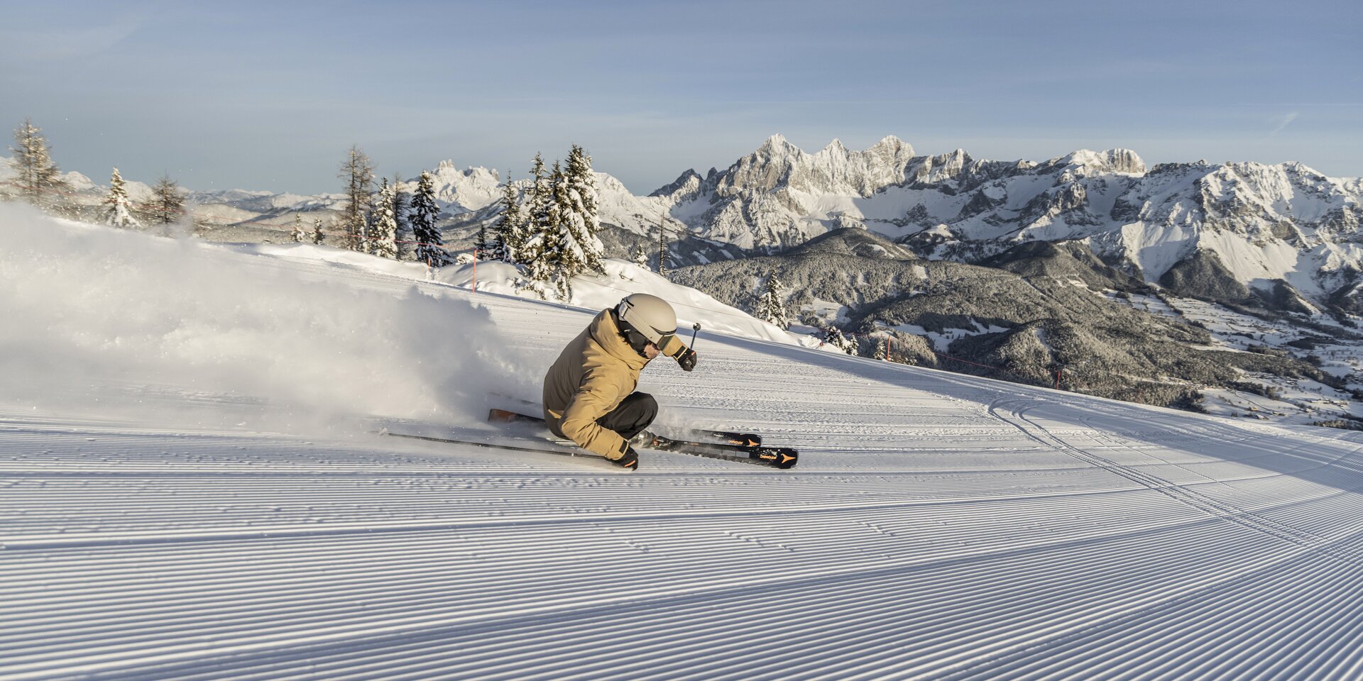 Skier carving on groomed slope with snowy mountains | © Mirja Geh