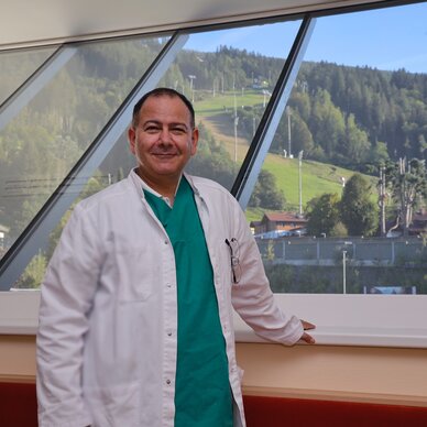 Medizinische Fachkraft im weißen Kittel vor großen Glasfenstern | © FotoTOM