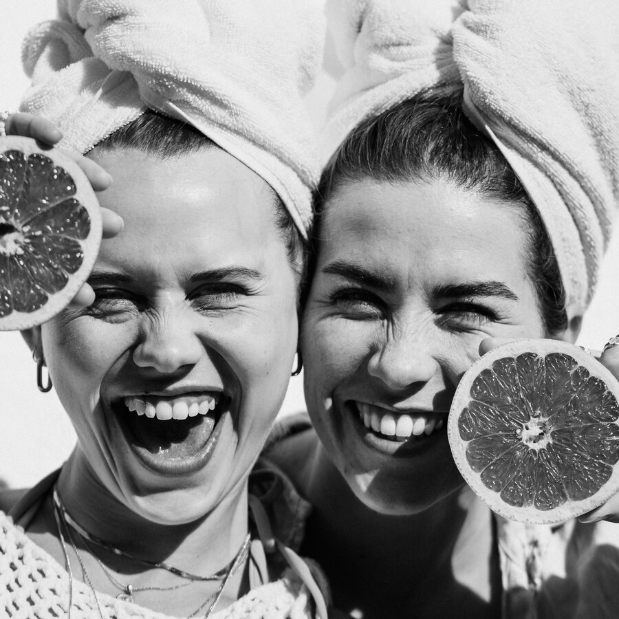 Two women with towels on their heads smiling, holding citrus halves