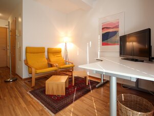 Wohnzimmer mit gelben Sesseln, weißem Schreibtisch und Fernseher | © SCHLADMING-APPARTEMENTS
