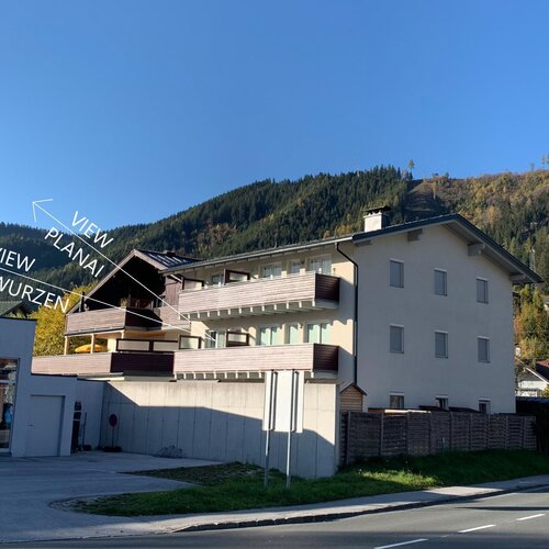 Modern residential building with balconies against forested mountains and blue sky