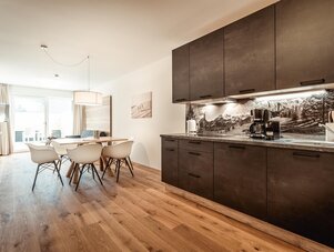 Modern kitchen with dark brown cabinetry, wooden flooring, and dining table.