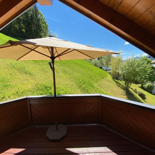 Wooden balcony with beige patio umbrella overlooking grassy hill