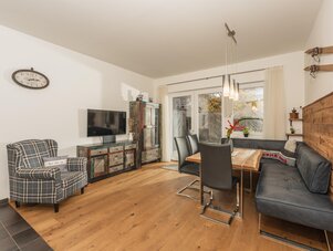 Living room with wooden floor, dining table, black chairs, and rustic cabinet