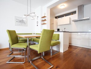 Dining area with green upholstered chairs and white kitchen