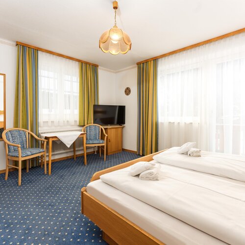 Hotel room with twin beds, table, chairs, and TV.