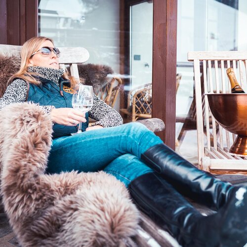 Woman lounging on a fur blanket outdoors with wine glass