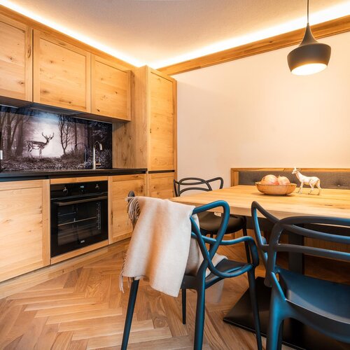 Wooden kitchen with cabinets, black countertop, oven, and dining table.