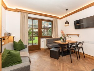 Living room with wooden floor, dining table, and garden view.