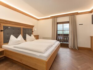 Hotel bedroom with a wooden bed, white bedding, and balcony view.