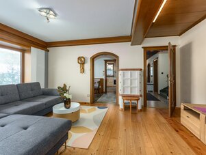 Gemütliches Wohnzimmer mit grauem Ecksofa, Holzböden und Deckenbalken