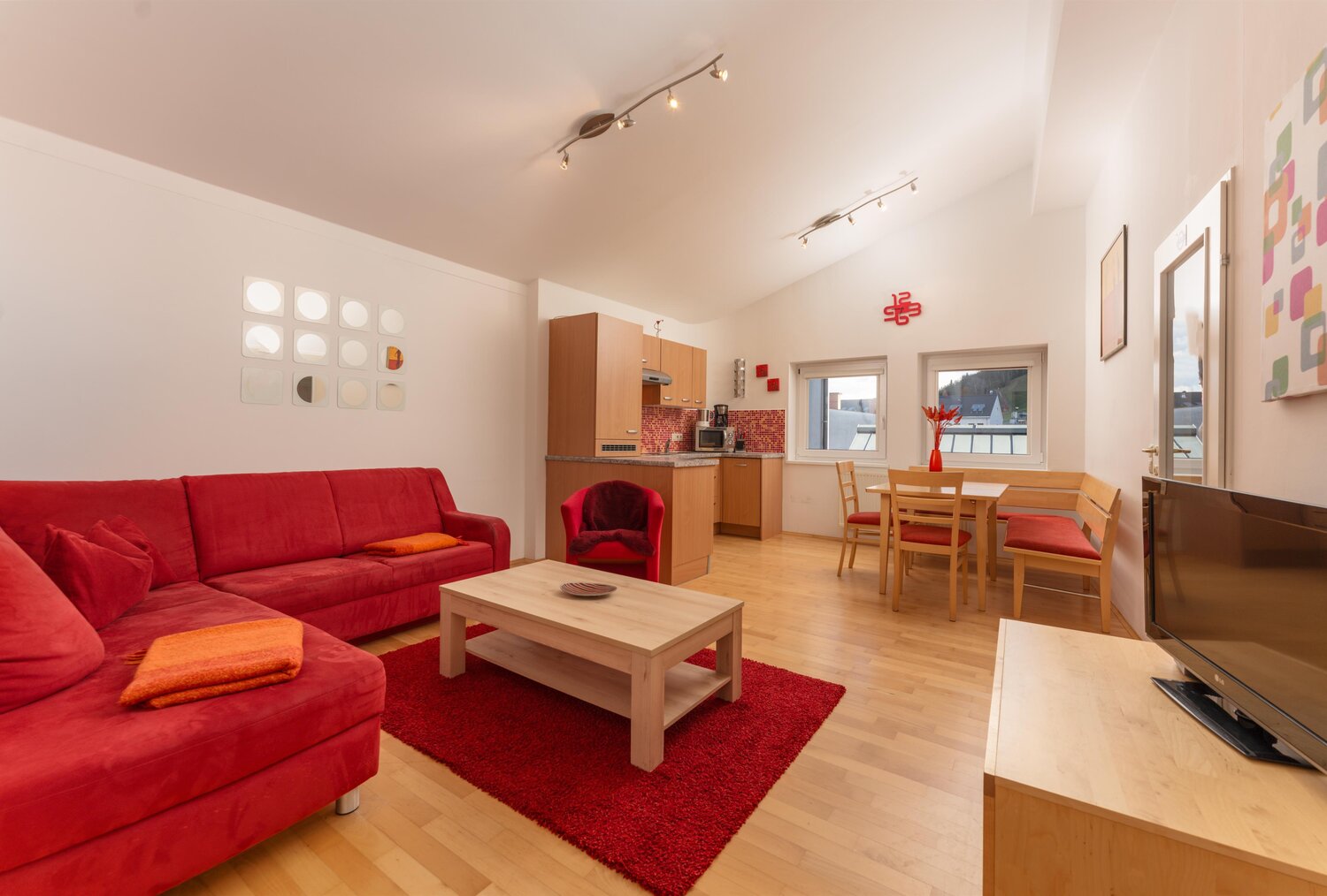 Bright living area with red sofa, dining table, and kitchenette