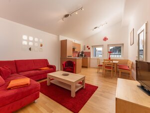 Bright living area with red sofa, dining table, and kitchenette.
