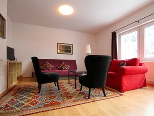 Living room with red sofa, two black armchairs, and colorful rug | © SCHLADMING-APPARTEMENTS