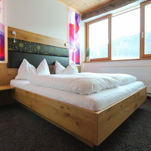Holzbett mit weißer Bettwäsche in hellem Hotelzimmer | © SCHLADMING-APPARTEMENTS