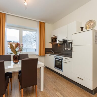 Modern white kitchen with oven, dining table, orange curtains