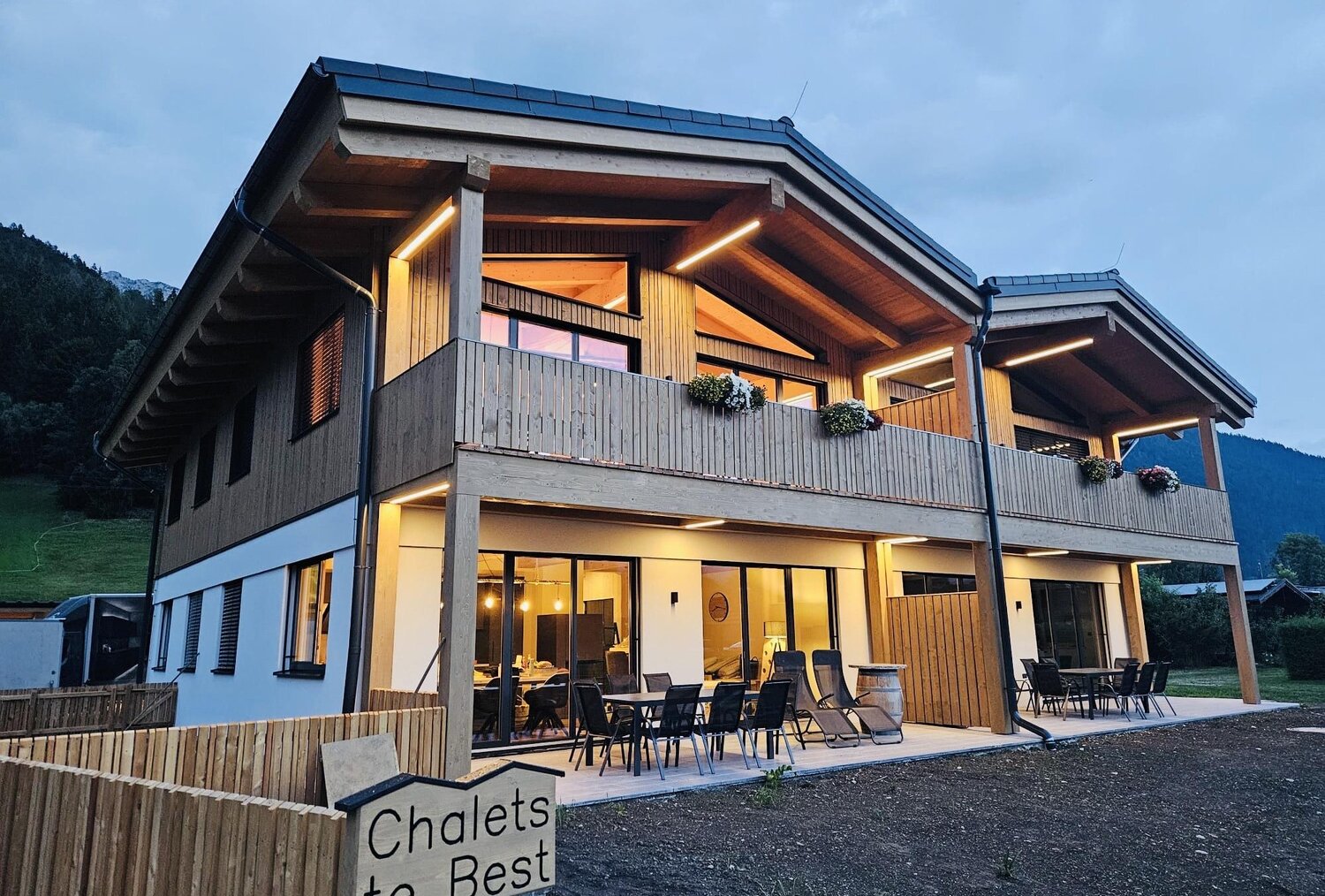 Two-story wooden chalet with balcony, outdoor seating at dusk.