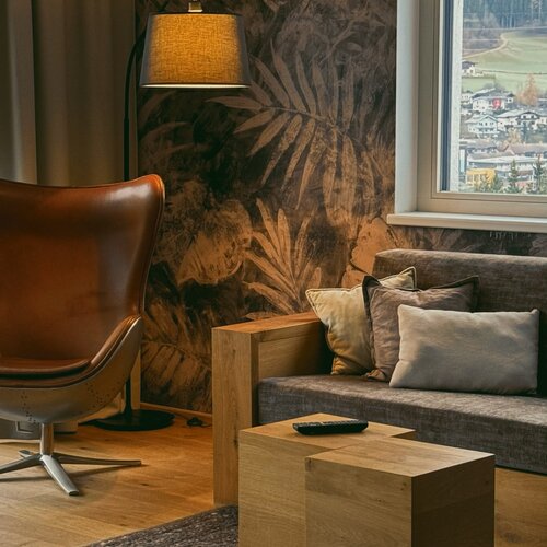 Cozy living room with leaf-pattern wallpaper, leather chair, and wooden cube tables