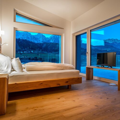 Hotel bedroom with wooden furniture and large windows overlooking mountains.