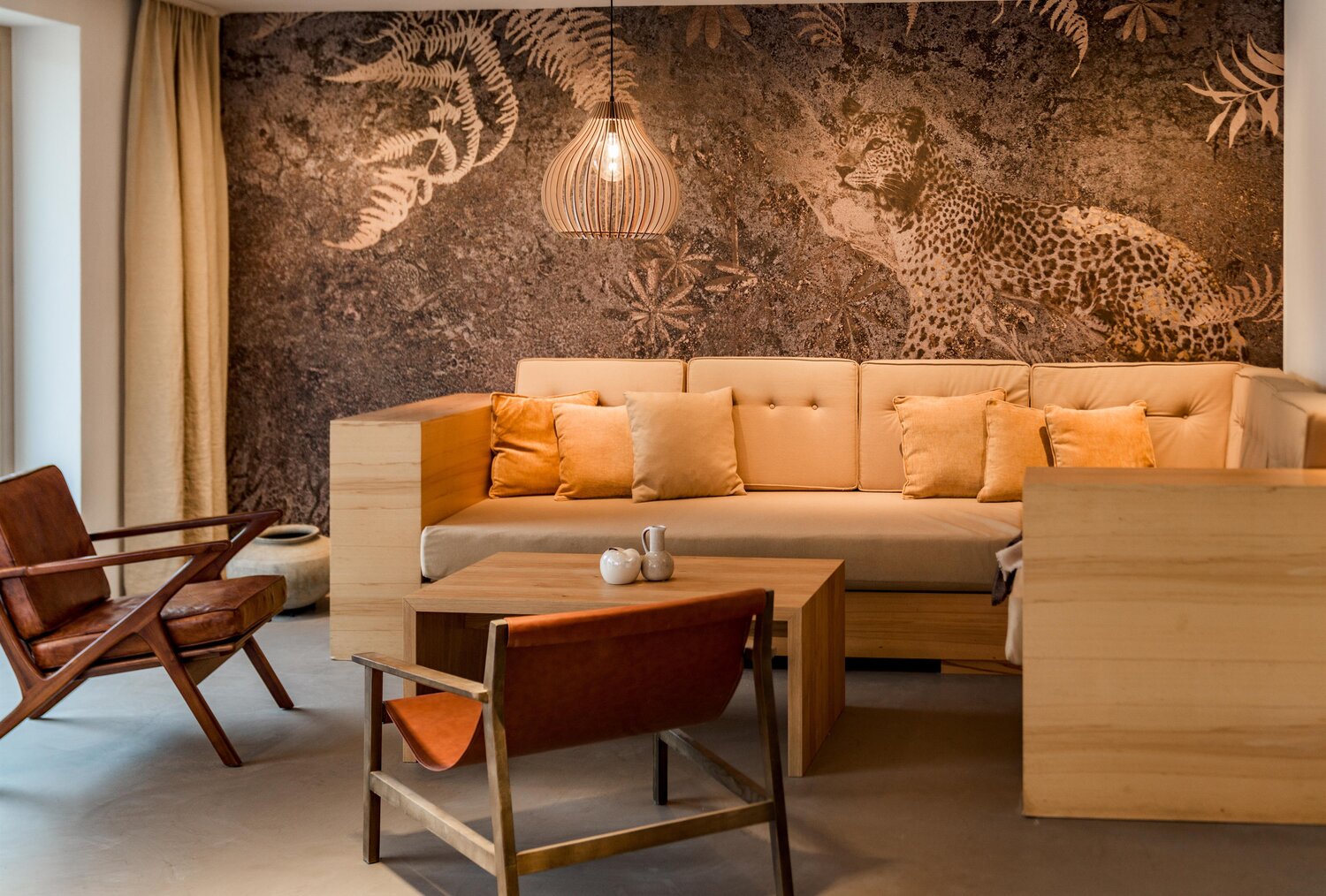 Cozy lounge area with beige sectional, wooden chairs, and a jungle mural.