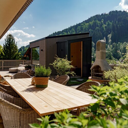 Sunlit outdoor terrace with wooden dining table, wicker chairs, and plants